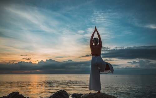 Eine Frau steht auf einem großen Stein an einem Gewässer und macht eine Yogapose. | © pixabay