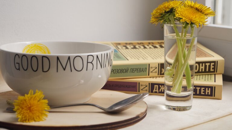 Good-Morning Tasse mit gelben Blumen und Büchern daneben. | © Unsplash