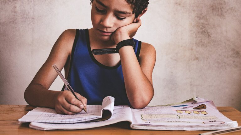 Junge, auf eine Hand gestützt, der an seinen Hausaufgaben sitzt | © pixabay