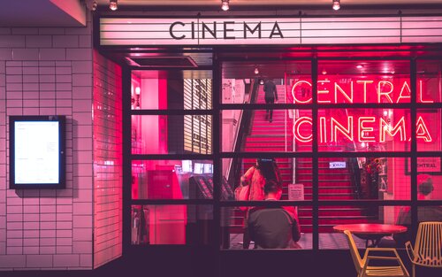 Blick von außen auf den Eingang eines Kinos, welches ein rotes Neonschild und rote Stufen hat. | © Myke Simon/unsplash