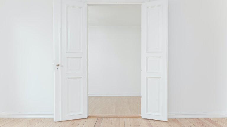 Die Perspektive ist von einem leeren Raum mit weißen Wände in einen anderen durch eine geöffnete weiße Flügeltür. | © Philipp Berndt/ unsplash