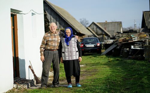 Ein älteres Ehepaar steht neben einem Haus, im Hintergrund steht ein Auto. | © unsplash