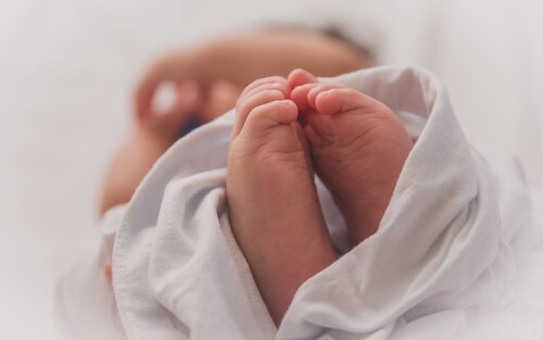 kleine Babyfüße schauen aus einem Tuch heraus, in das das Baby eingewickelt ist | © Luma Pimentel / Unsplash