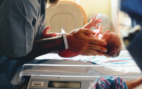 ein zu klein geborenes Baby wird von Männerhänden über einer Waage gehalten | © Christian Bowen / Unsplash
