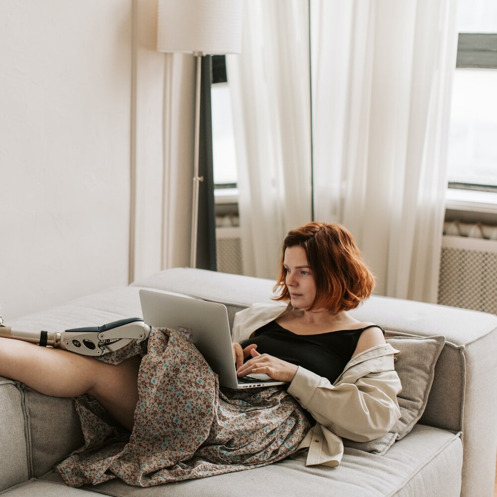 Eine Frau mit einer Beinprothese sitzt bequem auf einem Sofa und surft mit ihrem Laptop im Internet oder besucht unsere Community. | © Pexels / Vlada Karpovich