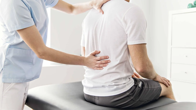 Eine Physiotherapeutin untersucht den Rücken eines männlichen Patienten in einer klinischen Umgebung. Der Mann im weißen T-Shirt sitzt mit dem Rücken zur Kamera. | © Pixabay