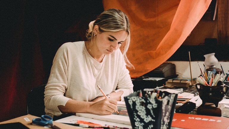 Eine Frau sitzt an einem Tisch und zeichnet ein Gemälde. | © Jonathan Borba/unsplash
