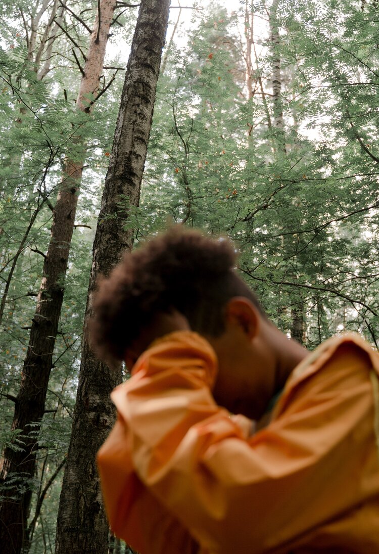 Ein Mann in orangener Jacke hält seine Hände an seine Stirn. Sein Blick ist auf den Boden gerichtet. Im Hintergrund ist ein Wald zu sehen. | © Ron Lach / Pexels.com