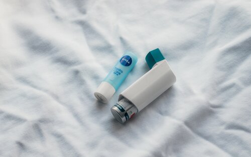 Ein Asthma Spray und ein Lippenpflegestift liegen auf einer Decke | © Unsplash