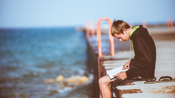 Ein Junge liest sitzend allein an einer Küste | © Ben White/unsplash