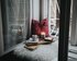 Eine gemütliche Ecke am offenen Fenster mit einer weißen Felldecke, einem Roten Kissen. Auf zei Holzbrettern stehen Bücher, eine Kerze und eine Tasse mit Kakao.  | © Alisa Anton/unsplash