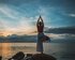 Eine Frau steht auf einem großen Stein an einem Gewässer und macht eine Yogapose. | © pixabay