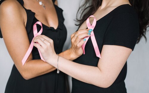Zwei Frauen-Oberkörper in schwarzem T-Shirt. Sie halten die vordere Hand überkreuzt und halten ein rosa Schleifchen in die Kamera | © Pexels Anna Tarazevich