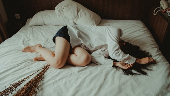 Eine Frau liegt niedergeschlagen im Bett und hält sich die Arme vors Gesicht. | © Yuris Alhumaydy/unsplash