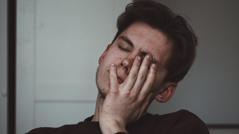 Ein erschöpfter Mann hält sich eine Hand vor sein Gesicht. | © unsplash