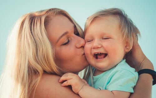 Eine Junge Mutter mit blonden Haaren hält ihr Baby im Arm und küsst es auf die Wange.  | © unsplash