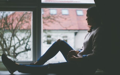 Frau sitzt in dunklem Raum im Fensterrahmen und blickt nach draußen | © pixabay