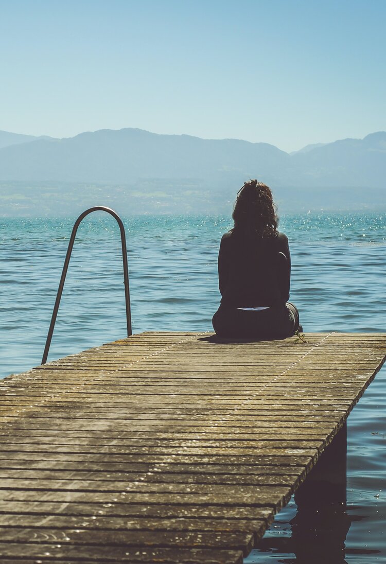 Eine Frau sitzt auf einem Bootssteg und schaut auf das Meer. | © Paola Chaaya/ Unsplash