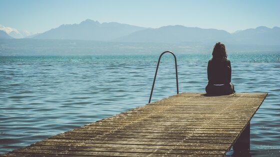 Eine Frau sitzt auf einem Bootssteg und schaut auf das Meer. | © Paola Chaaya/ Unsplash