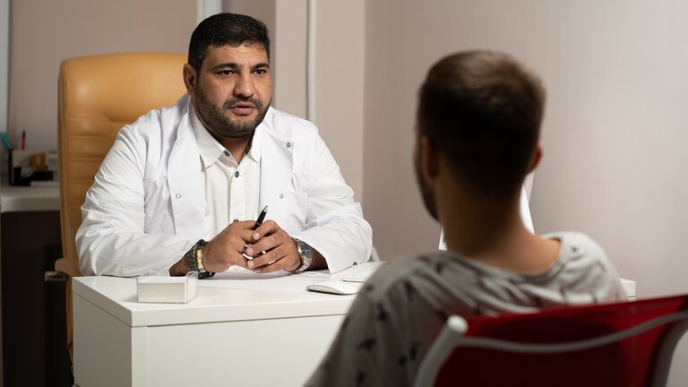 Ein Arzt im weissen Kittel sitzt an seinem Schreibtisch und hört seinem Patienten geduldig zu. | © Pixabay