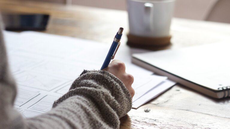 ein Arm mit einem Stift in der Hand, eine Person schreibt in ein Tagebuch | © unsplash