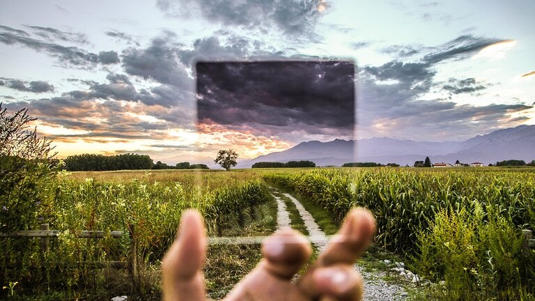 ein Filter von einer Hand festgehalten vergrößert im Hintergrund ein Maisfeld im Sonnenuntergang | © Pixabay