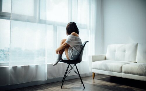 Foto von einer Frau mit dunklen Haaren, die auf einem Stuhl sitzt und aus dem Fenster schaut. | © Unsplash