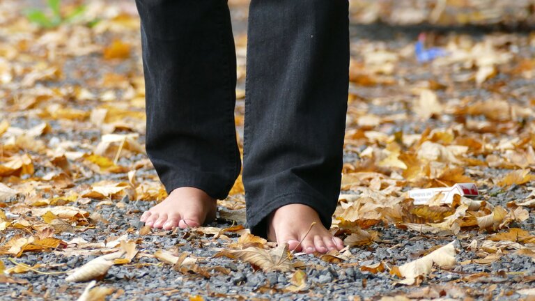 Beine einer Person, die eine schwarze Hose trägt und barfuß über einen Kiesweg läuft | © unsplash