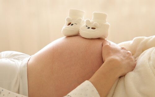 Eine Frau liegt auf dem Rücken. Man sieht den Babybauch auf dem gehäkelte Babyschuhe stehen. | © pixabay