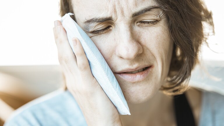 eine Frau mit schmerzverzerrtem Gesicht, die einen Eisbeutel an ihren Kiefer hält | © pixabay