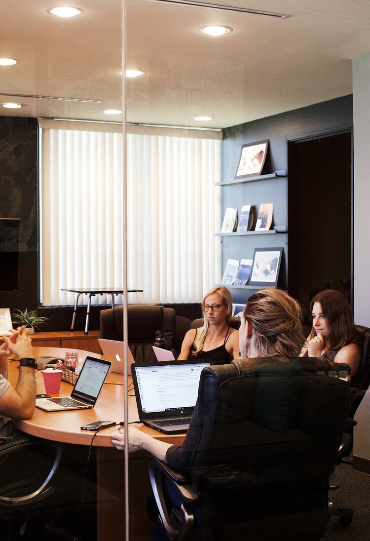 Hinter einer Glastür sitzen vier Personen an einer Seite eines Konferenztischs. Vor ihnen stehen Laptops. | © unsplash