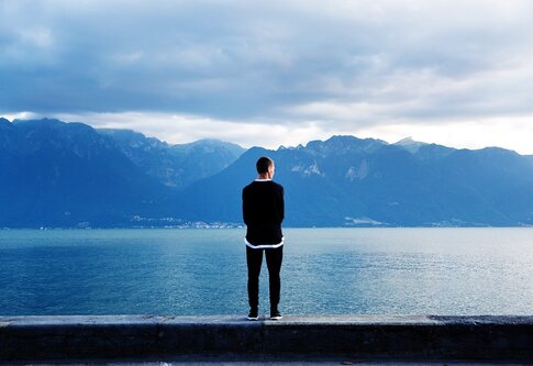 Mann von hinten, der auf Mauer steht und auf einen See blickt | © pixabay