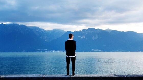Mann von hinten, der auf Mauer steht und auf einen See blickt | © pixabay