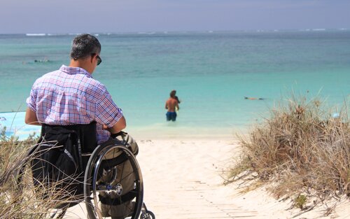 Ein Mann sitzt im Rollstuhl an einem Strand und blickt auf das Meer. | © pixabay