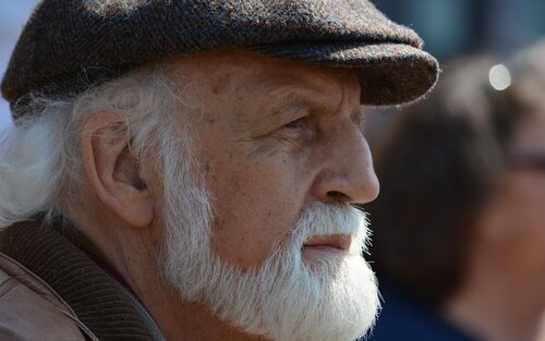 Gesicht eines älteren Mannes im Seitenprofil. Er trägt einen braunen Hut und eine braune Jacke. Er hat weiße Haare sowie einen Bart. | © pixabay