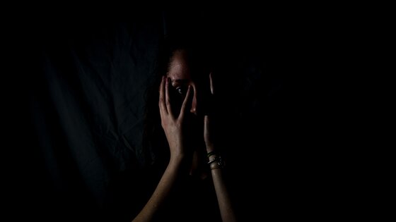 Frau im Dunkeln hält sich die Hände vors Gesicht | © Melanie Wasser/unsplash