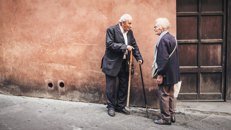 Zwei ältere Personen stehen vor einem Haus und unterhalten sich | © Christina Gottardi/unsplash