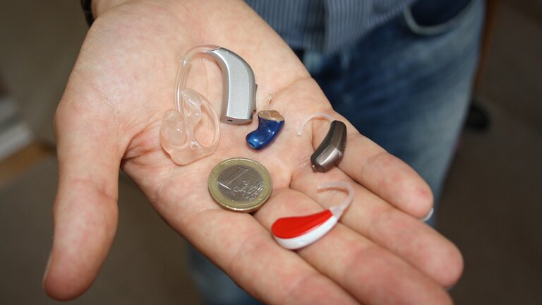 verschiedene Hörgeräte liegen zum Vergleich mit einer 1 Euro Münze auf einer Hand | © pixabay
