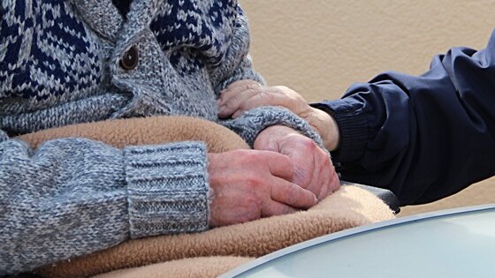 die Hände eines Rollstuhlfahrers liegend auf dessen Schoß werden von einer weiteren Person gehalten | © pixabay