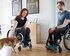 Eine junge Frau und ein junger Mann, jeweils im Rollstuhl, sitzen mit ihrem kleinen Hund in einem Flur ihrer rollstuhlgerechten Wohnung | © adira.de, Fotograf: Daniel George