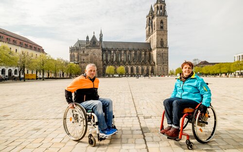 Zwei Personen im Rollstuhl posieren auf einem Platz vor dem Dom in Magdeburg.  | © Magdeburg Marketing, Andreas Lander