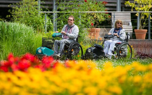 Eine Frau und ein Mann fahren mit ihren Rollstühlen durch den Park in Bad Bevensen, an einem rot-gelbem Blumenfeld vorbei. | © Lars Wendlandt