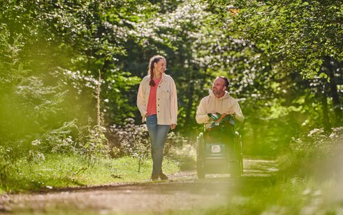 Eine Frau geht mit einem Mann im Rollstuhl im Wald spazieren. | © Jens Wegner, Tourismus Zentrale Saarland TZS