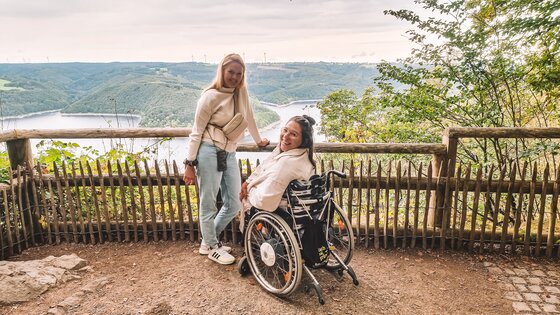Zwei Frauen, eine linkst im Bild stehend die andere rechts daneben im Rollstuhl sitzend, befinden sich auf einer Aussichtsplattform. | © Wheeliewanderlust