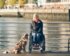 Eine Rollstuhlfahrerin posiert mit ihrem Hund auf einer Brücke in der Hafenstadt Hamburg mit der Elbphilharmonie im Hintergrund. | © Lukas Kapfer/Hamburg Tourismus GmbH