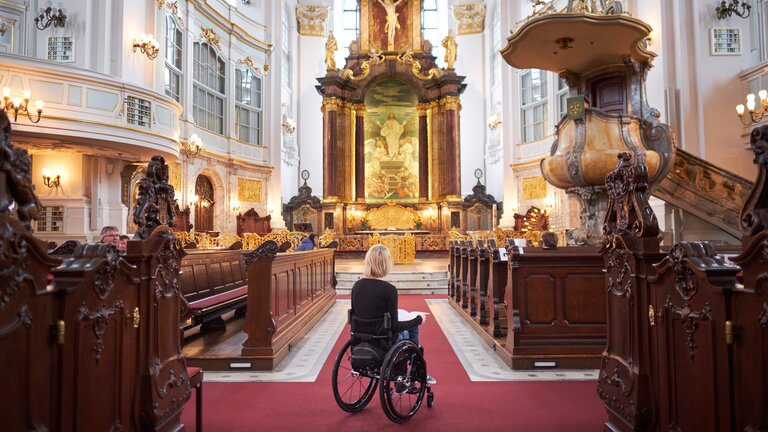 Eine Rollstuhlfahrerin im Innenraum der St. Michaeliskirche, von hinten, blickt auf den Altarraum. | © Lukas Kapfer/Hamburg Tourismus GmbH