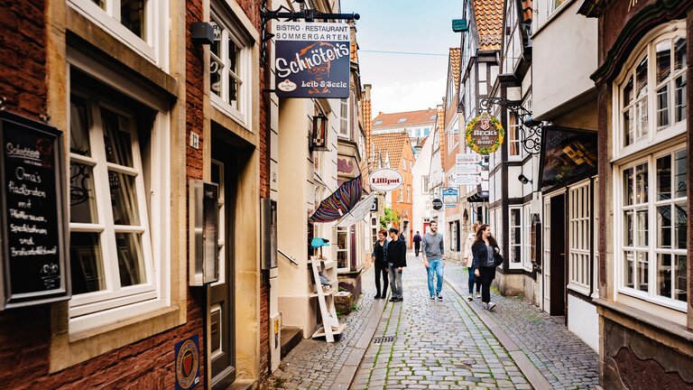 Eine schmale und historische Gasse mit Geschäften und Restaurants auf beiden Seiten. Menschen gehen die Straße entlang und betrachten die Schaufenster. | © WFB/Jonas Ginter