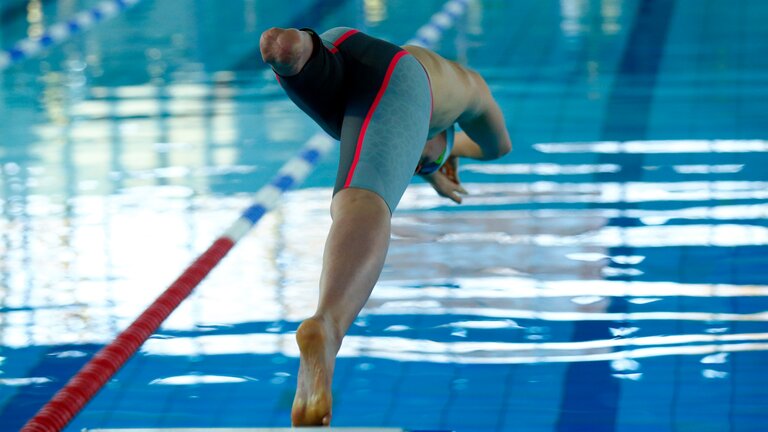 Einbeiniger Schwimmer springt vom Startblock mit dem Kopf voran ins Schwimmbecken | © picture alliance / DBS