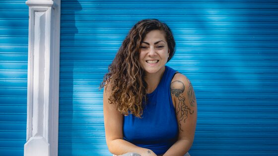 Samira mit breitem Lächeln vor einer blauen Wand. | © Erik Schütz/GoodBY