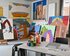 Im Vordergrund steht ein großer Tisch mit Pinseln, Farben und Zeichnungen. Im Hintergrund lehnen an der Wand Leinwände mit fertigen Werken. | © kaethe:k Kunsthaus